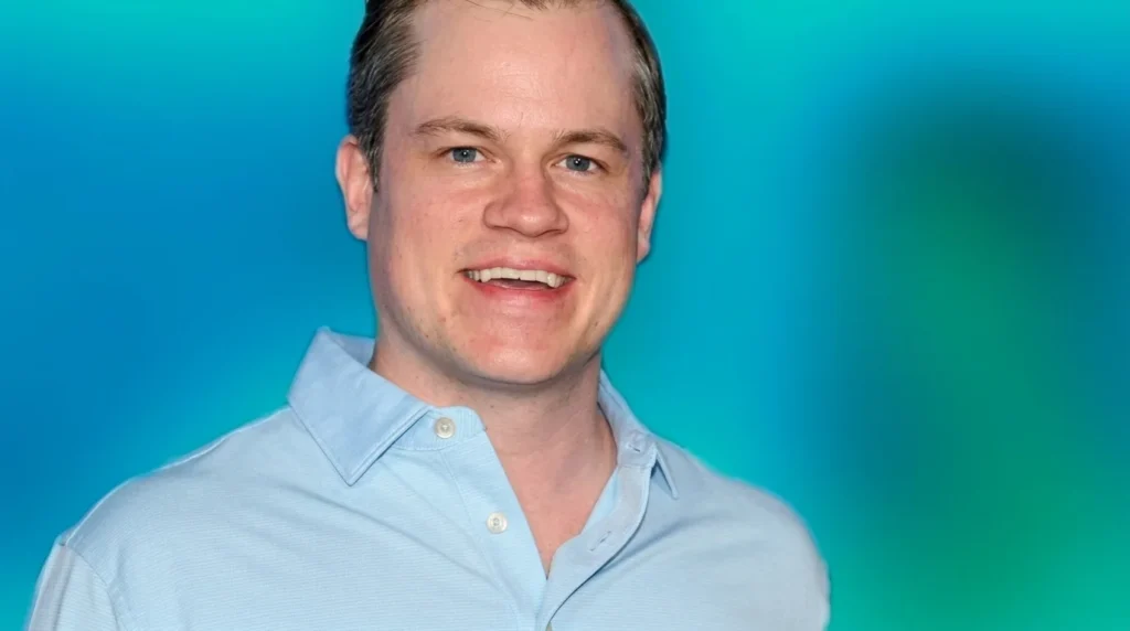 A close-up portrait of Jett Puckett smiling against a bright blue gradient background