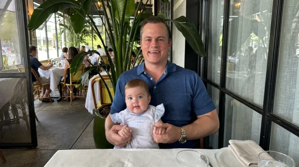 Jett Puckett holding a baby while seated at a dining table inside a restaurant